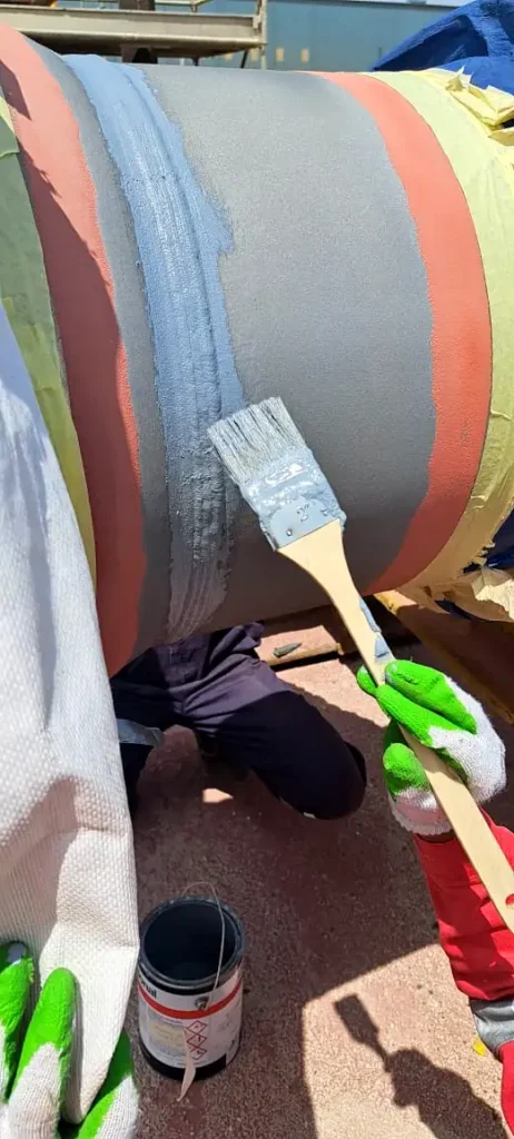 Worker applying stripe coat by brush on weld area before full coating application.